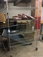Full view of the rolling metal wire shelving unit with four shelves, holding some cushions (contents not included).
