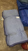Six stacked blue cushioned moving blankets with zigzag padding and blue binding on edges