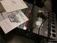 Photo showing the motorized saw top with attached power cord and table surface, and scattered instruction manuals.