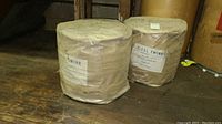 Two large rolls of sisal twine wrapped in plastic on wooden reels placed on a wooden floor, viewed from side angle.