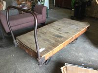 Full view of the large wood and metal vintage cart with metal handle and wheels on concrete floor.