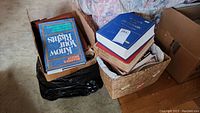 Multiple books stacked in two boxes and a basket, showing titles and condition.