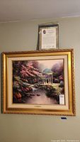 Full view of the framed Thomas Kinkade print on the wall with certificate of authenticity above.