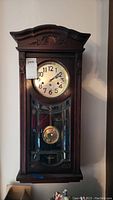 Full front view of the wooden grandmother clock showing the overall shape, clock face, and glass front with pendulum.