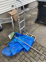 Magliner utility handtruck folded down with blue tarp, broom, and dustpan on patio.