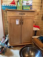 Front view of wooden kitchen cart showing drawer, cabinet doors, and casters on floor.