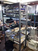 Angle showing one shelving unit fully loaded with various papers, model bus boxes, and other basement items. Shelving frame is gray metal, with four shelves approximately 36 inches wide, 24 inches deep, and 75 inches tall.