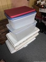 Stack of clear and colored-lid plastic storage bins and lids stacked in basement area.