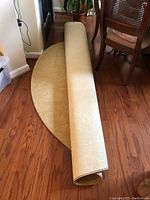 Rolled and unrolled view of the beige round area rug showing the soft texture and subtle floral embossing on the surface, placed on hardwood floor near dining chairs.