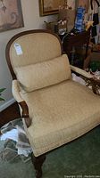 Front angled view of beige upholstered Lexington armchair with wooden frame and rounded back.