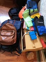 Various backpacks and travel bags stacked, including leather and canvas bags with bright colored dry bags