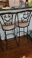 Pair of metal framed bar chairs with decorative scrollwork backs and beige suede seats positioned at kitchen counter.