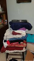 Stack of folded clothing including scarves, sweaters, jackets, and t-shirts in various colors.