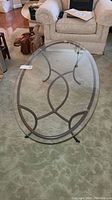 Full view of the oval glass top coffee table showing the clear glass and metal frame with intersecting circular design.