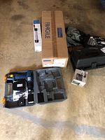 Ryobi cordless drill set with charger, battery, and gray carrying case, plus a tall box labeled fragile for tripod.