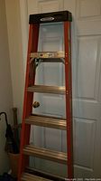 Full view of Werner 6-foot fiberglass stepladder leaning against white door showing aluminum steps and black tool tray on top.