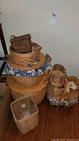 Photo showing multiple woven Longaberger baskets stacked, including a round picnic basket with padded floral liner and a smaller basket on top.