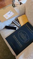 Large black portfolio cover titled ‘Eyewitness to History’ and ‘Barack Obama Road to the White House’ alongside envelopes and pen box on couch