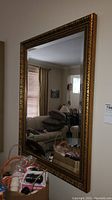 Full view of the framed wall mirror showing its rectangular shape, clear reflective glass, and ornate gold frame.