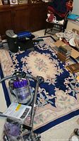 Full view of the blue area rug with floral design in a room with some items on and around it.