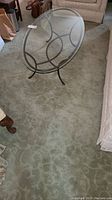 Photo showing a close-up view of the green patterned area rug under a glass-top coffee table, highlighting the subtle swirl pattern and plush texture.