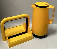 Yellow plastic thermos standing next to yellow acrylic napkin holder with black handle