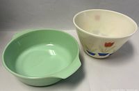 Two vintage mixing bowls, one jadeite green with a pour spout and one tulip patterned off-white bowl.