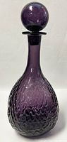 Side view of purple textured glass decanter with round lid