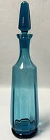 Front view of the teal blue ribbed glass decanter with stopper in place.