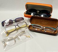 Six pairs of eyeglasses including prescription and non-prescription styles placed on a white surface with two cases.