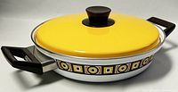 Side view showing yellow enamel lid, black handles, and geometric patterned metal pan body.