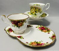 Two Royal Albert teacup and saucer sets shown, one with yellow flower pattern and the other with rose floral pattern and sandwich plate.