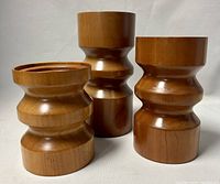 Front view of three teak nesting pillar candleholders showing their sculptural turned designs