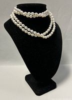 Front and full length view of a 3-wrap pearl necklace displayed on black velvet stand.