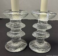 Front view of pair of textured clear glass candleholders holding white candles.