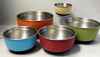 Five nested mixing bowls showing different colored enamel exteriors and stainless steel interiors with non-slip bottoms visible.