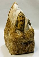 Front view of the carving showing the human figure's face with hood and engraved patterns of feathers on clothing and eagle's wings.