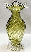 Front view of olive green blown glass vase with spiral swirl design, ruffled clear glass rim, and scalloped clear glass base.
