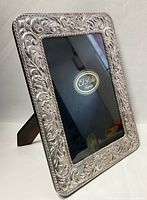 Front angled view showing the ornate floral and leaf embossed sterling silver frame with black interior for photo insert, with El Polo Argento branding inside.