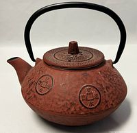 Front side view of the cast iron teapot showing coin motifs and black handle