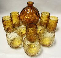 Top view of 9 amber glasses with 7-inch decanter in center showing textured circular designs on decanter and glasses.