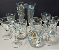 Group photo showing all glassware pieces with blue and gold atomic amoeba design on clear glass, including pilsner beer glasses, stemmed whiskey glasses, stemless whiskey glasses, and assorted stemware mugs.