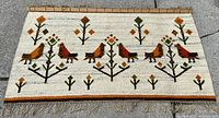 Full view of wall hanging rug laid flat on pavement showing complete bird and tree motif with fringe at bottom