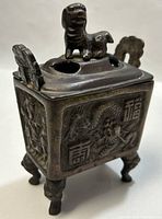 Angled close-up of the bronzed incense burner showing embossed dragon design and Foo Dog finial on lid.