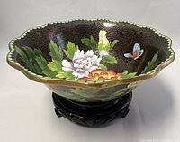 Front angled view showing interior cloisonné floral and butterfly design, scalloped rim, and wooden base.