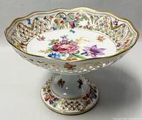 Side angle view showing reticulated pierced lattice sides, golden scalloped edges, colorful floral centerpiece and pedestal base with more floral decoration.