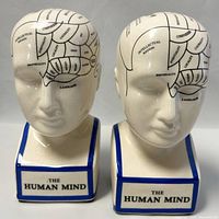 Front and side views of two ceramic phrenology head coin banks labeled 'The Human Mind'.