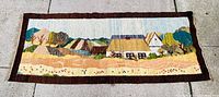 Full view of the rectangular rug showing the entire folk art pastoral scene with fields, cottages, and trees.