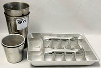 Photo showing set of four metal drinking cups, two taller and two shorter, all silver-colored stainless steel with minor wear.
