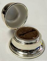 Ring holder with open lid showing brown felt interior for ring storage.